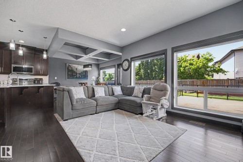Open-concept living area featuring dark wood-finish flooring, a coffered ceiling, and a kitchen island with white countertop - 1944 68 Street, Edmonton, AB 