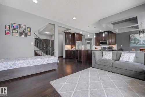 Open-concept living area featuring dark wood-finish flooring, a kitchen with dark cabinetry and stainless steel appliances, a breakfast bar, recessed lighting, and a coffered ceiling detail - 1944 68 Street, Edmonton, AB 