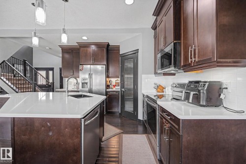 Contemporary kitchen featuring dark wood-finish cabinetry, stainless steel appliances, white countertops, and a subway tile backsplash - 1944 68 Street, Edmonton, AB 