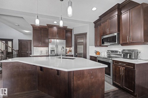 Spacious kitchen featuring a large central island with a white countertop, dark wood-finish cabinetry, stainless steel appliances, and pendant lighting - 1944 68 Street, Edmonton, AB 