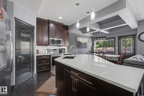 Kitchen featuring a large central island with a solid surface countertop, dark wood cabinetry, stainless steel appliances, and wood-finish flooring - 1944 68 Street, Edmonton, AB 