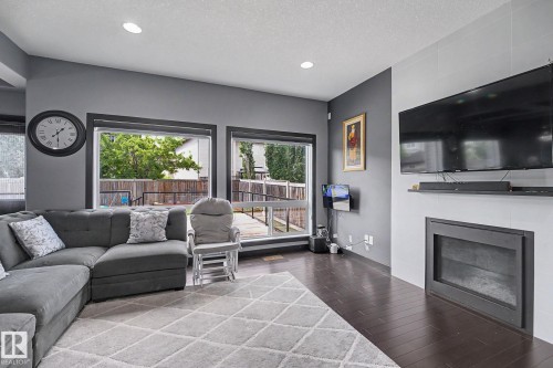 Spacious living area featuring dark wood-finish flooring, a modern fireplace with a sleek surround, and multiple large windows - 1944 68 Street, Edmonton, AB 