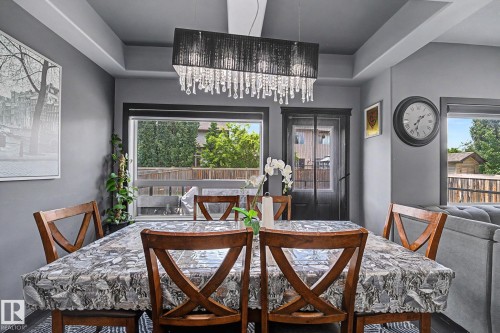 Dining area featuring a contemporary chandelier with crystal accents, tray ceiling, and dual windows - 1944 68 Street, Edmonton, AB 