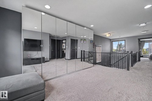 Upper-level landing featuring wall-to-wall carpeting, recessed ceiling lighting, a mirrored wall, and a staircase with dark wood railings and black metal balusters - 1944 68 Street, Edmonton, AB 