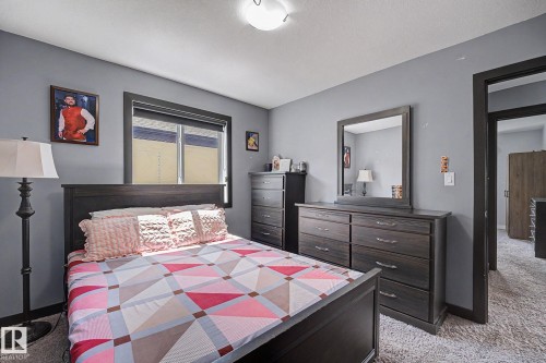 Carpeted bedroom featuring a window with roller shades, a dark wood-finish door frame, a ceiling-mounted light fixture, and light gray wall paint - 1944 68 Street, Edmonton, AB 
