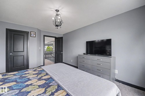 Bedroom featuring a dark-tone chandelier, two dark-paneled doors, and gray walls - 1944 68 Street, Edmonton, AB 