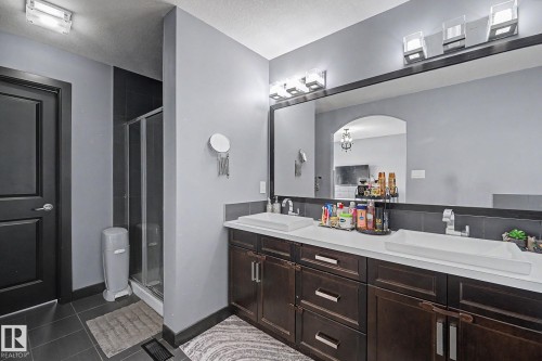 Double vanity featuring vessel sinks, white countertops, dark wood cabinetry, and an expansive wall-mounted mirror - 1944 68 Street, Edmonton, AB 