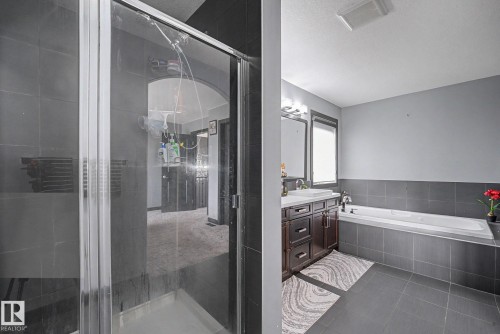Contemporary bathroom featuring a spacious walk-in shower with glass enclosure, a white soaking tub, and a dual vanity with dark wood-finish cabinetry - 1944 68 Street, Edmonton, AB 