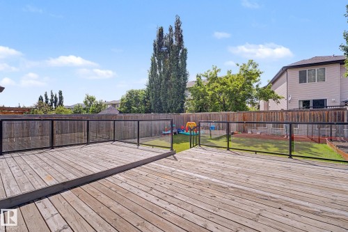 Spacious wooden deck featuring a glass and metal railing, overlooking a fenced backyard with a lawn and raised garden beds - 1944 68 Street, Edmonton, AB 