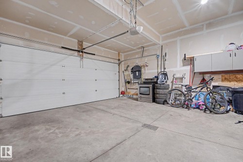 Attached garage featuring a white sectional overhead door with an automatic opener, exposed drywall walls, concrete flooring, and overhead lighting - 1944 68 Street, Edmonton, AB 
