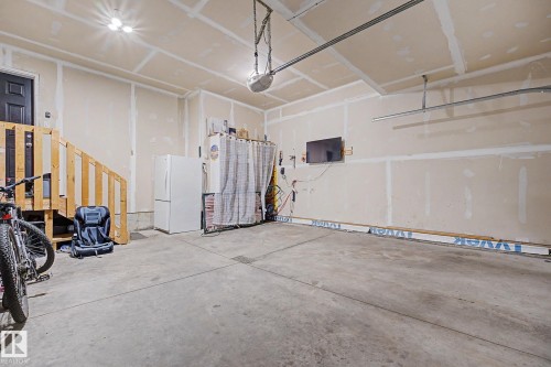 Spacious garage featuring a concrete floor, exposed drywall, overhead lighting, and an access door with a wooden staircase - 1944 68 Street, Edmonton, AB 