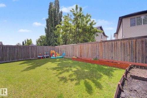 Expansive backyard featuring a manicured lawn, full privacy fencing, and raised garden beds - 1944 68 Street, Edmonton, AB 