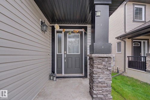 Inviting entryway featuring a dark gray door with sidelight, light gray siding, a black overhead soffit, and a stone-clad pillar - 1944 68 Street, Edmonton, AB 