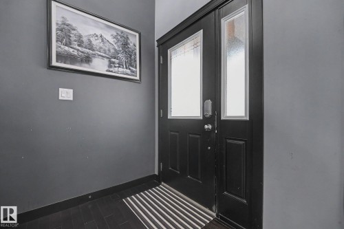 Black paneled door with glass inserts and an adjacent sidelight, featuring dark wood-finish flooring and grey wall tones - 1944 68 Street, Edmonton, AB 