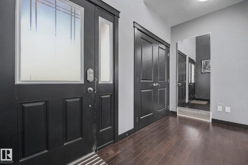 Entryway featuring a dark wood-finish door with decorative glass inserts, coordinating dark wood-finish flooring, a built-in full-length mirror, and light gray wall paint - 1944 68 Street, Edmonton, AB 