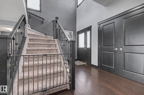 Elegant foyer featuring dark wood-finish flooring, a carpeted staircase with dark iron balusters, and a front entry door with sidelights - 1944 68 Street, Edmonton, AB 