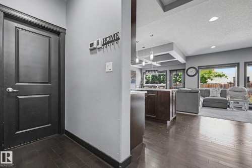 Dark wood-finish flooring extending into an open-concept living space with large windows, recessed lighting, and a coffered ceiling detail - 1944 68 Street, Edmonton, AB 