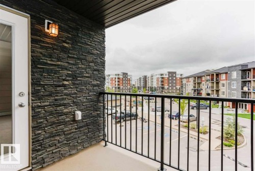 Balcony featuring a dark stacked stone accent wall, exterior wall sconce, and black metal railing - 328 3315 James Mowatt Trail, Edmonton, AB 