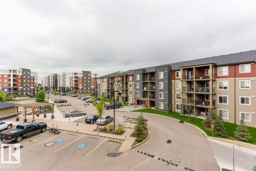 Apartment complex exterior featuring multiple buildings with balconies, paved parking areas, a landscaped driveway, and a wood pergola - 328 3315 James Mowatt Trail, Edmonton, AB 