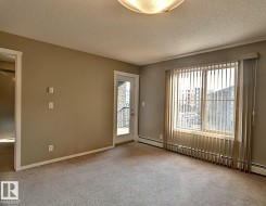 Neutral-toned carpeted room featuring a large window with vertical blinds, a glass-paneled door leading to a balcony with wrought iron railing, and a flush mount ceiling light fixture - 