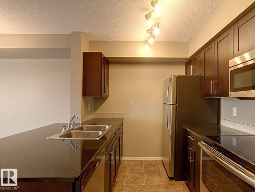 Modern kitchen featuring dark wood-finish cabinetry and dark countertops - 328 3315 James Mowatt Trail, Edmonton, AB 