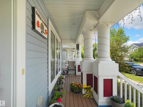 Covered porch featuring light blue siding, white trim, wood-finish flooring, and multiple white columns with red bases - 7827 22 Avenue, Edmonton, AB 
