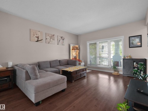 Spacious living area featuring rich wood-finish flooring and ample natural light from a large bay window - 7827 22 Avenue, Edmonton, AB 