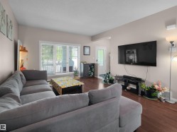 Spacious living area featuring warm wood-finish flooring, a large picture window with blinds, and neutral wall tones - 