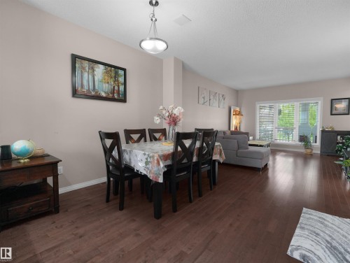 Expansive open-concept living area featuring wood-finish flooring, a contemporary chandelier, and a large window - 7827 22 Avenue, Edmonton, AB 
