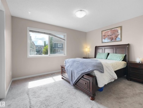 Carpeted bedroom featuring a large window, neutral wall paint, and a flush-mount ceiling light fixture - 7827 22 Avenue, Edmonton, AB 