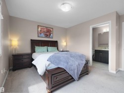 Carpeted bedroom featuring a dark wood-finish bed frame, two matching dark wood-finish nightstands, a ceiling-mounted light fixture, and an entry to a bathroom with a dark wood-finish vanity - 