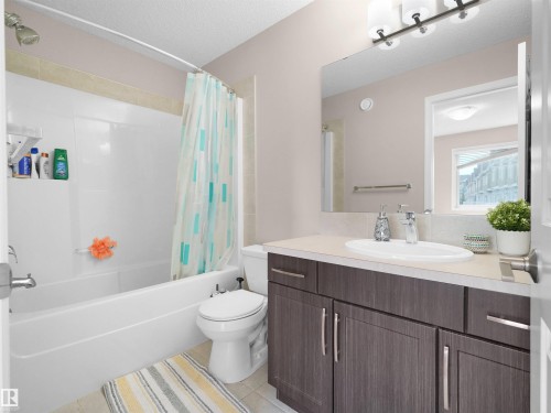 Bathroom featuring a tub/shower combination with a shower head, a single vanity with a white oval basin, a light-toned countertop, and dark wood-finish cabinetry with silver hardware - 7827 22 Avenue, Edmonton, AB 