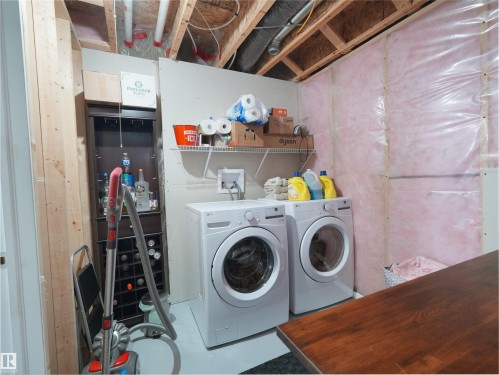 Laundry area featuring a front-loading washer and dryer set, wire shelving, and exposed ceiling joists - 7827 22 Avenue, Edmonton, AB 