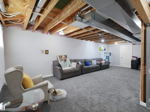 Finished basement space featuring light gray walls, plush gray carpeting, exposed ceiling joists, and visible ductwork - 7827 22 Avenue, Edmonton, AB 