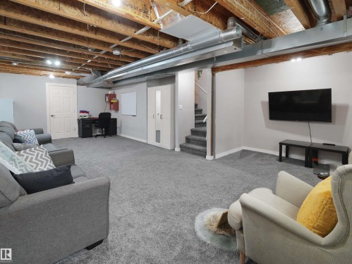 Spacious finished area featuring light gray carpeting, neutral wall tones, recessed lighting, and exposed ceiling joists - 7827 22 Avenue, Edmonton, AB 
