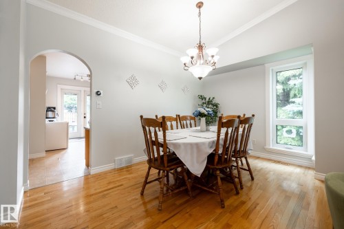 Dining space featuring wood-finish flooring, a contemporary chandelier, and a large window - 27 Danforth Crescent, St. Albert, AB 