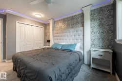 Bedroom featuring a tufted upholstered headboard, accent wallpaper, crown molding with cove lighting, and a ceiling fan - 