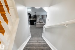 Carpeted stairs with white wooden railings descend to a lower level featuring light gray walls, a window, and recessed ceiling lighting - 