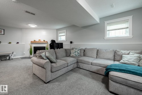 Carpeted lower level featuring a fireplace with a wood mantel and shiplap-style wall, built-in recessed lighting, and a chair rail - 27 Danforth Crescent, St. Albert, AB 