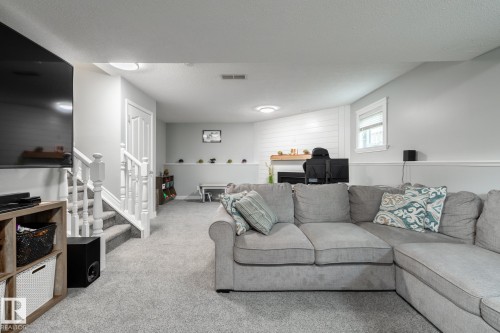 Finished lower level featuring light gray walls, plush carpeting, white trim, a built-in fireplace with a wood mantle, and a window - 27 Danforth Crescent, St. Albert, AB 