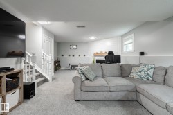 Finished lower level featuring light gray walls, plush carpeting, white trim, a built-in fireplace with a wood mantle, and a window - 