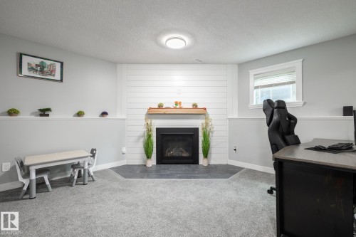 Carpeted room featuring a fireplace with a wood mantle and shiplap surround, a single window, and a built-in shelf with trim - 27 Danforth Crescent, St. Albert, AB 