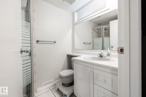 Bathroom featuring a glass-enclosed shower, white vanity with integrated sink, white tile flooring, and mirrored medicine cabinet - 27 Danforth Crescent, St. Albert, AB 