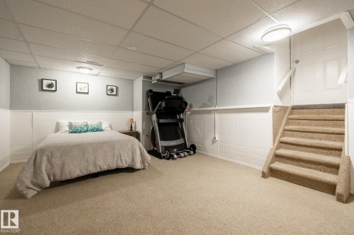 Carpeted room with white paneling and light blue walls, featuring a drop ceiling with recessed lighting and flush mount fixtures, and a carpeted stairway with white railing - 27 Danforth Crescent, St. Albert, AB 