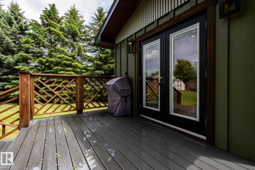Composite decking with a decorative wood railing, framed by mature evergreens - 27 Danforth Crescent, St. Albert, AB 