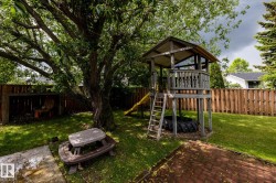 Expansive backyard featuring a lush lawn, mature shade tree, privacy fencing, and a brick paver patio area - 
