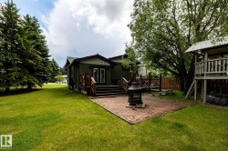 Expansive backyard featuring a red brick patio, green lawn, mature trees, and a wooden deck with railing - 