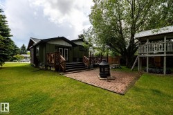 Spacious backyard featuring a brick paver patio with a central fire pit, extensive green lawn, and mature trees - 