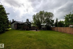 Spacious rear yard featuring extensive lawn area, mature trees, and a full privacy fence - 