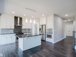 Kitchen featuring white cabinetry, dark stone countertops, stainless steel appliances, a mosaic tile backsplash, and wood-finish flooring - 